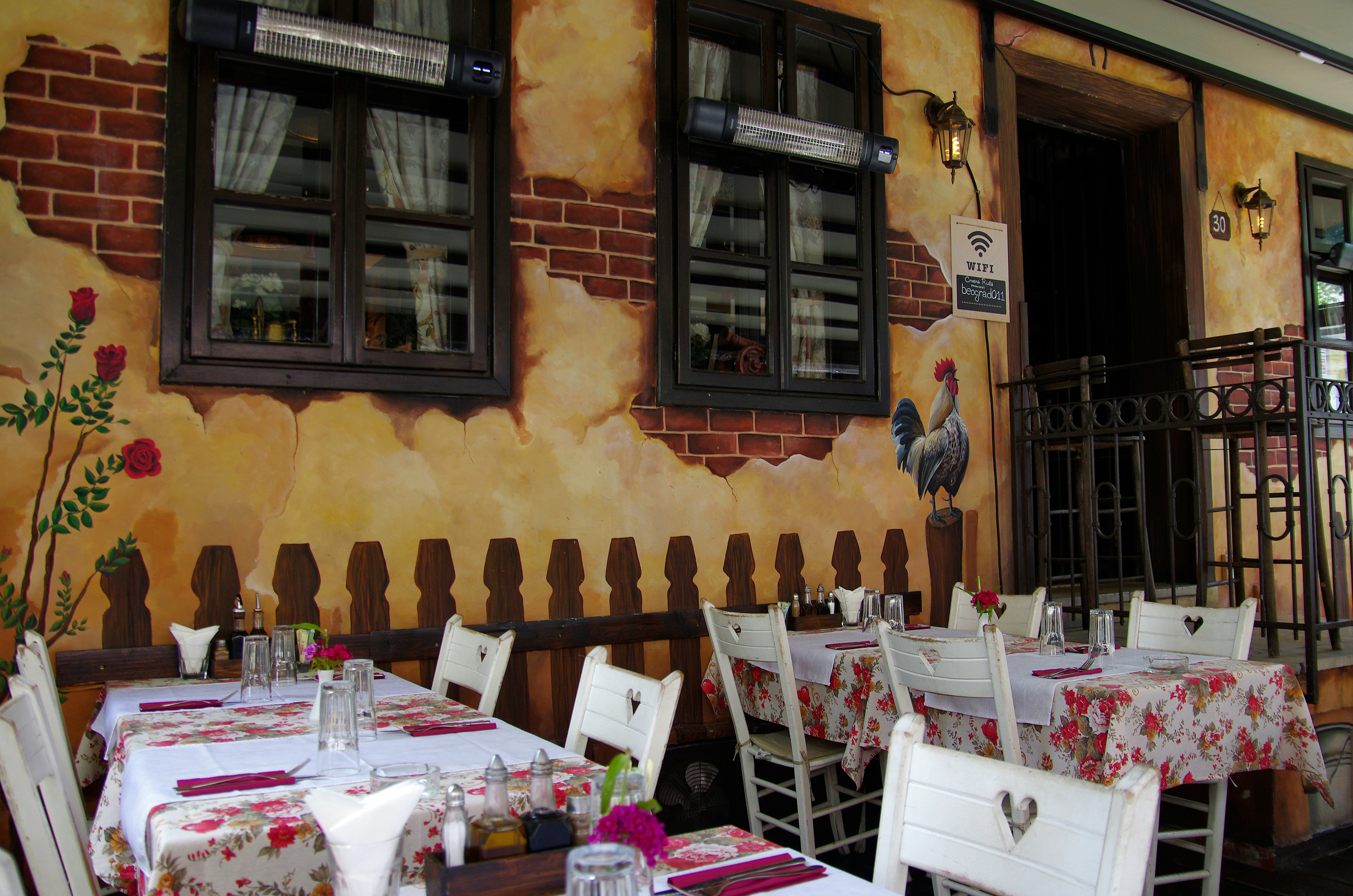 Outdoor terrace of a Belgrade kafana with floral tablecloths and painted mural wall