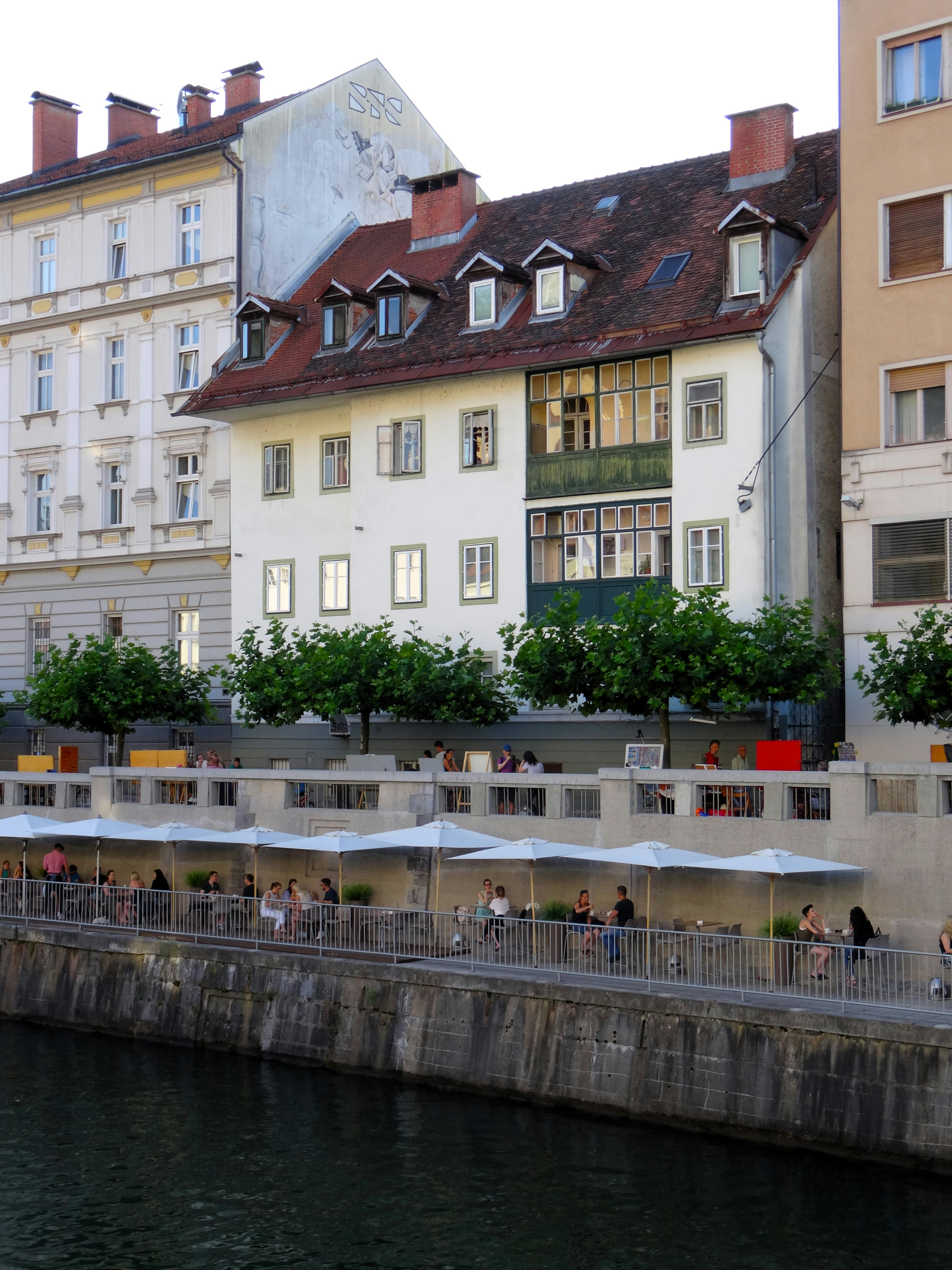 Outdoor restaurant terraces along the Ljubljanica river in Ljubljana, Slovenia, with historic buildings rising behind