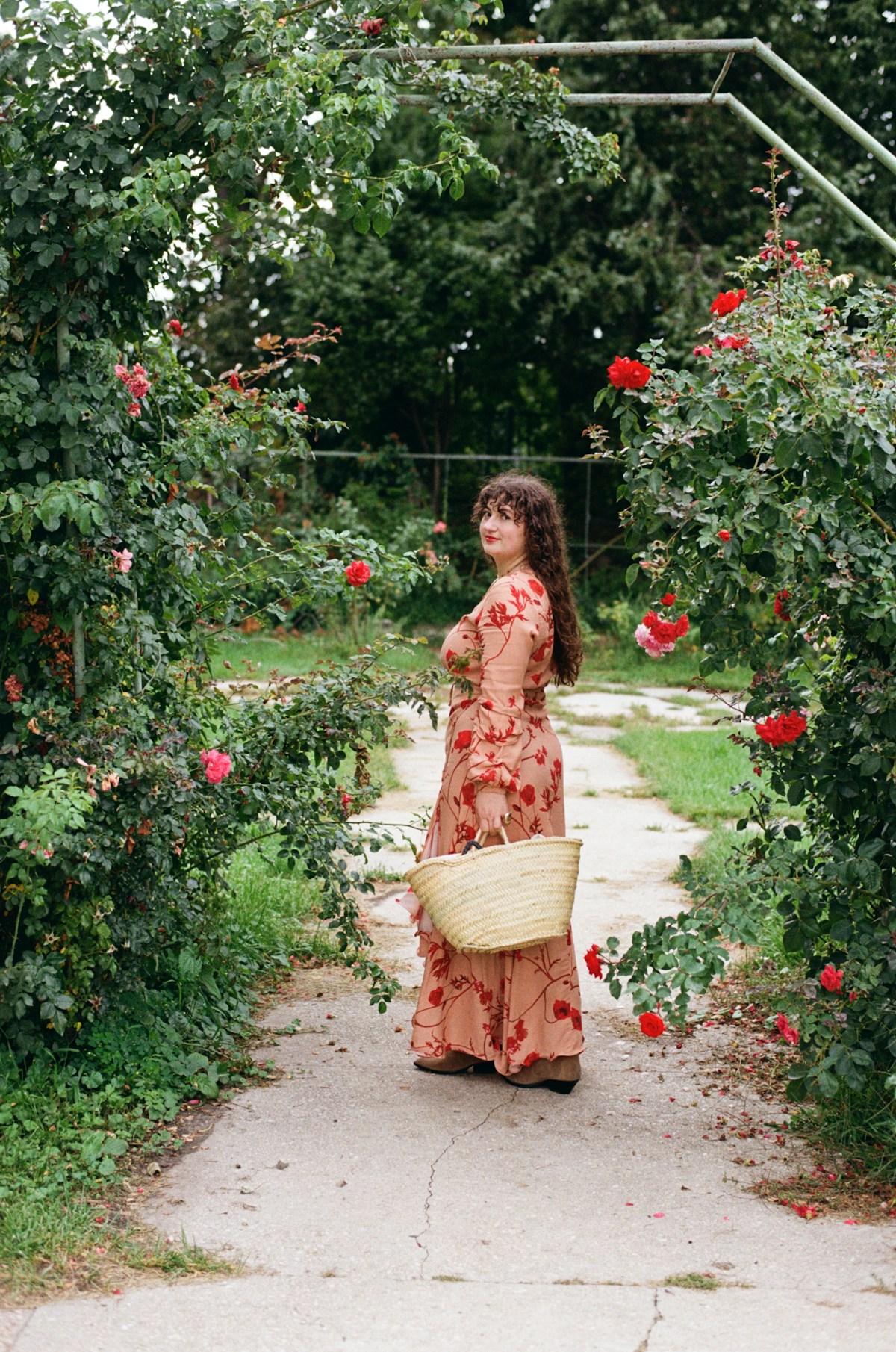 Woman in a floral dress with a basket walking through a rose garden
