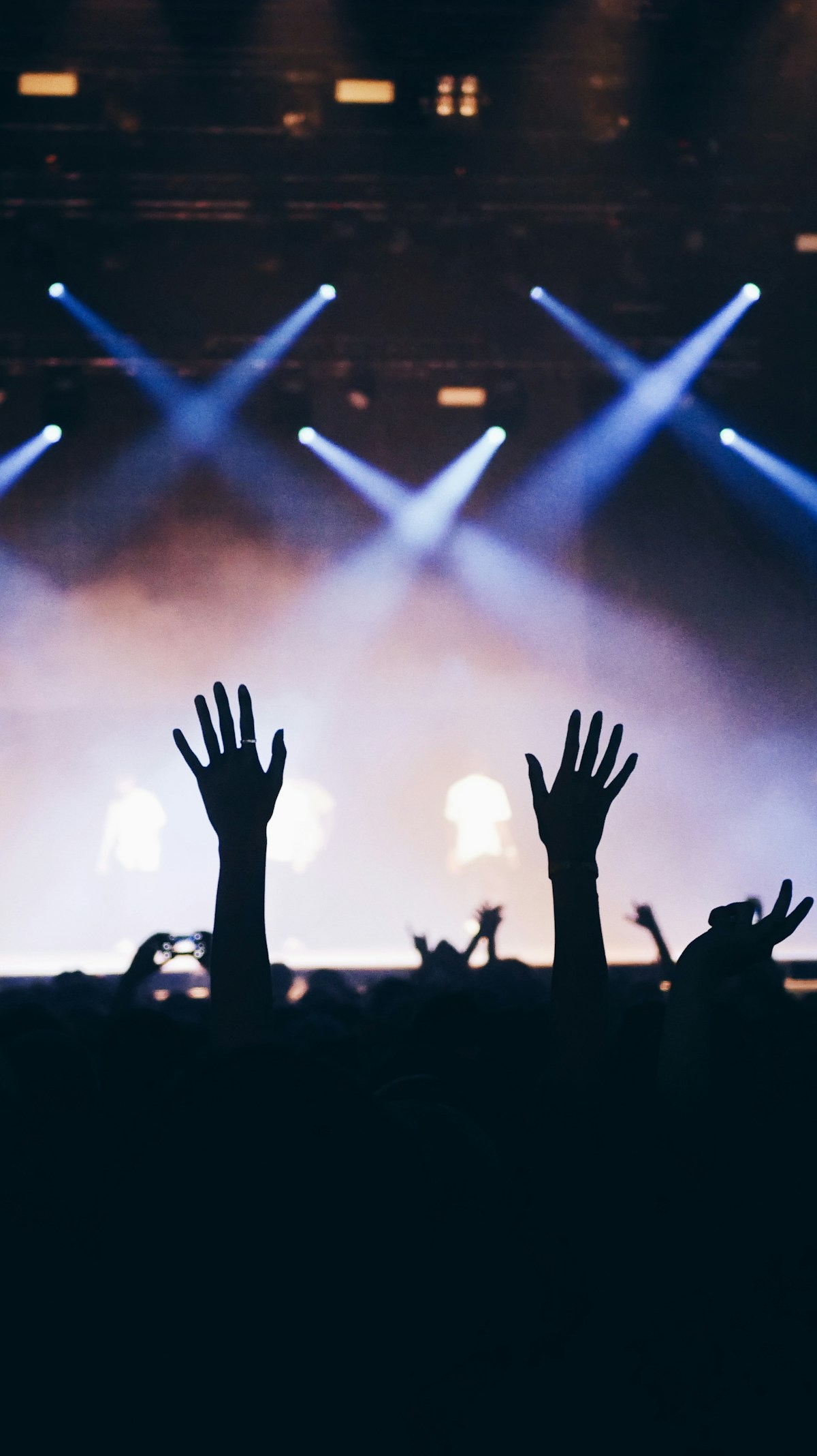 Silhouette of concert crowd with raised hands against stage lights