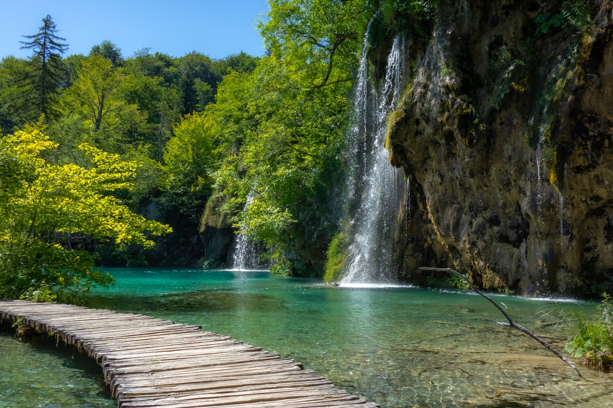 Wooden boardwalk on turquoise lake with waterfalls and trees at Plitvice Lakes, Croatia