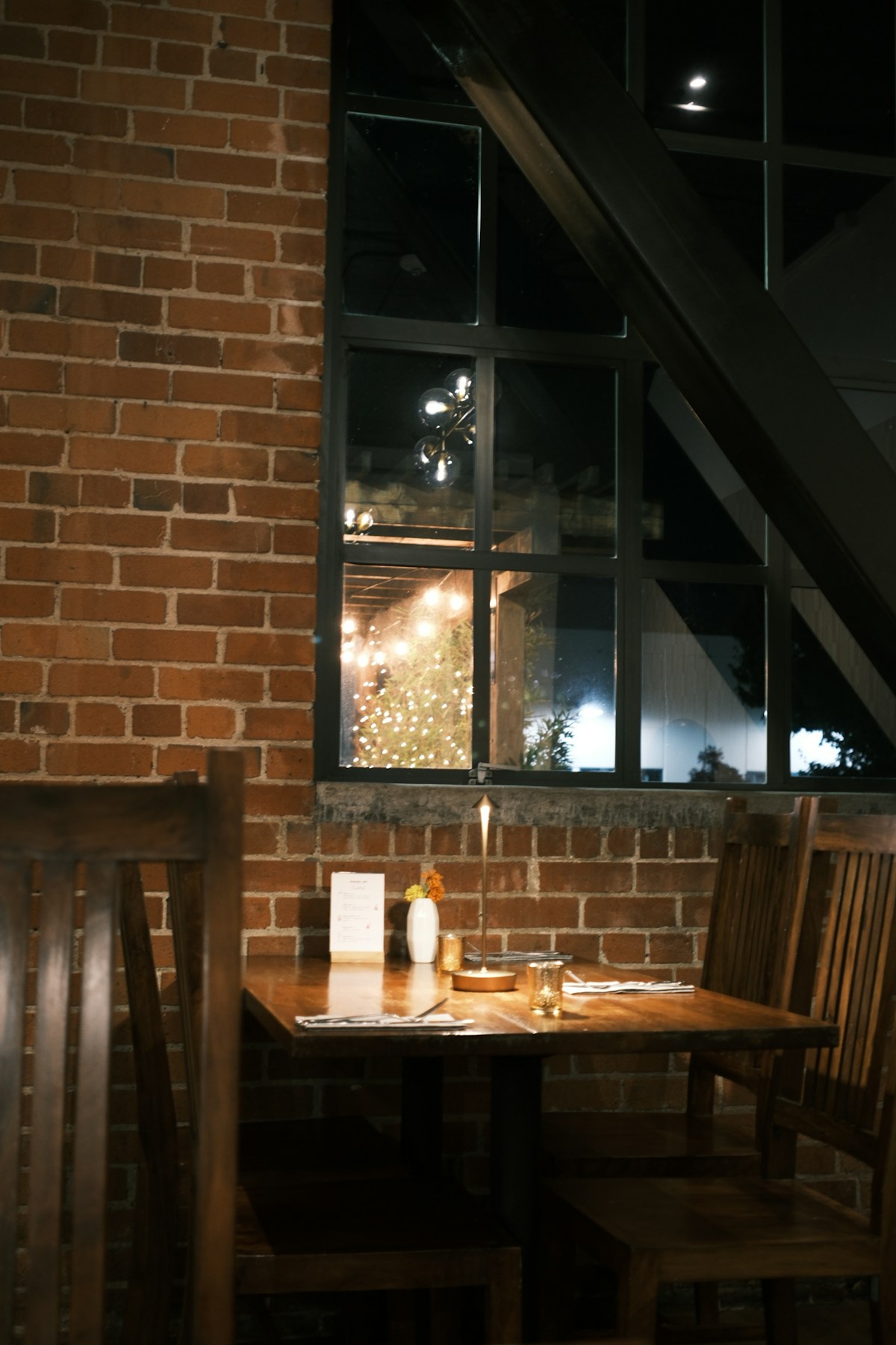 Cosy restaurant interior with exposed brick wall, candlelit wooden table, and window looking onto evening lights