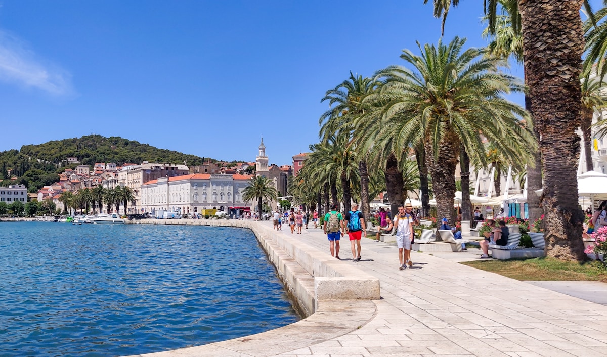 People walking along the Split waterfront promenade with palm trees, Croatia