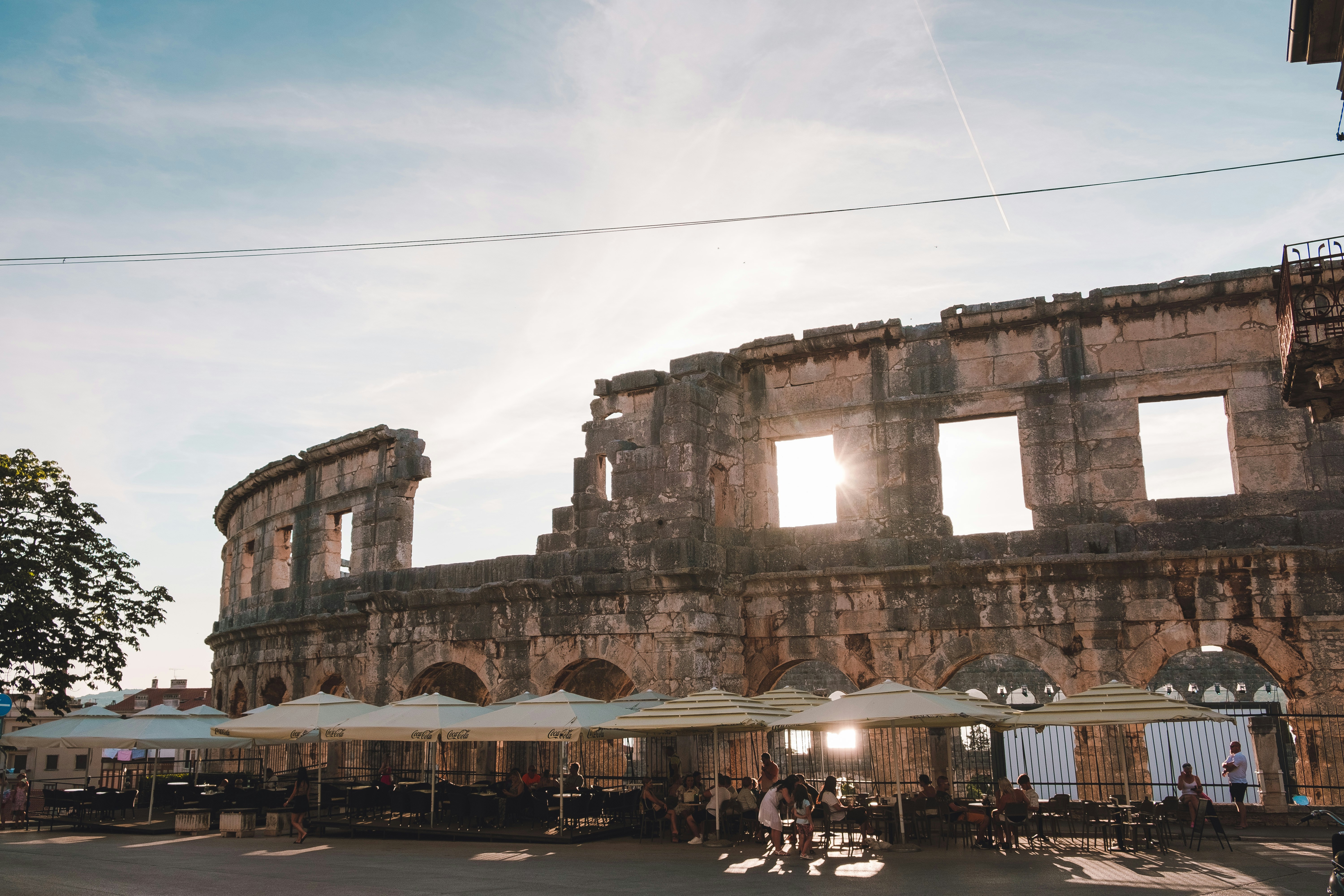 Outdoor restaurant tables with sun umbrellas in front of Pula Arena, Croatia