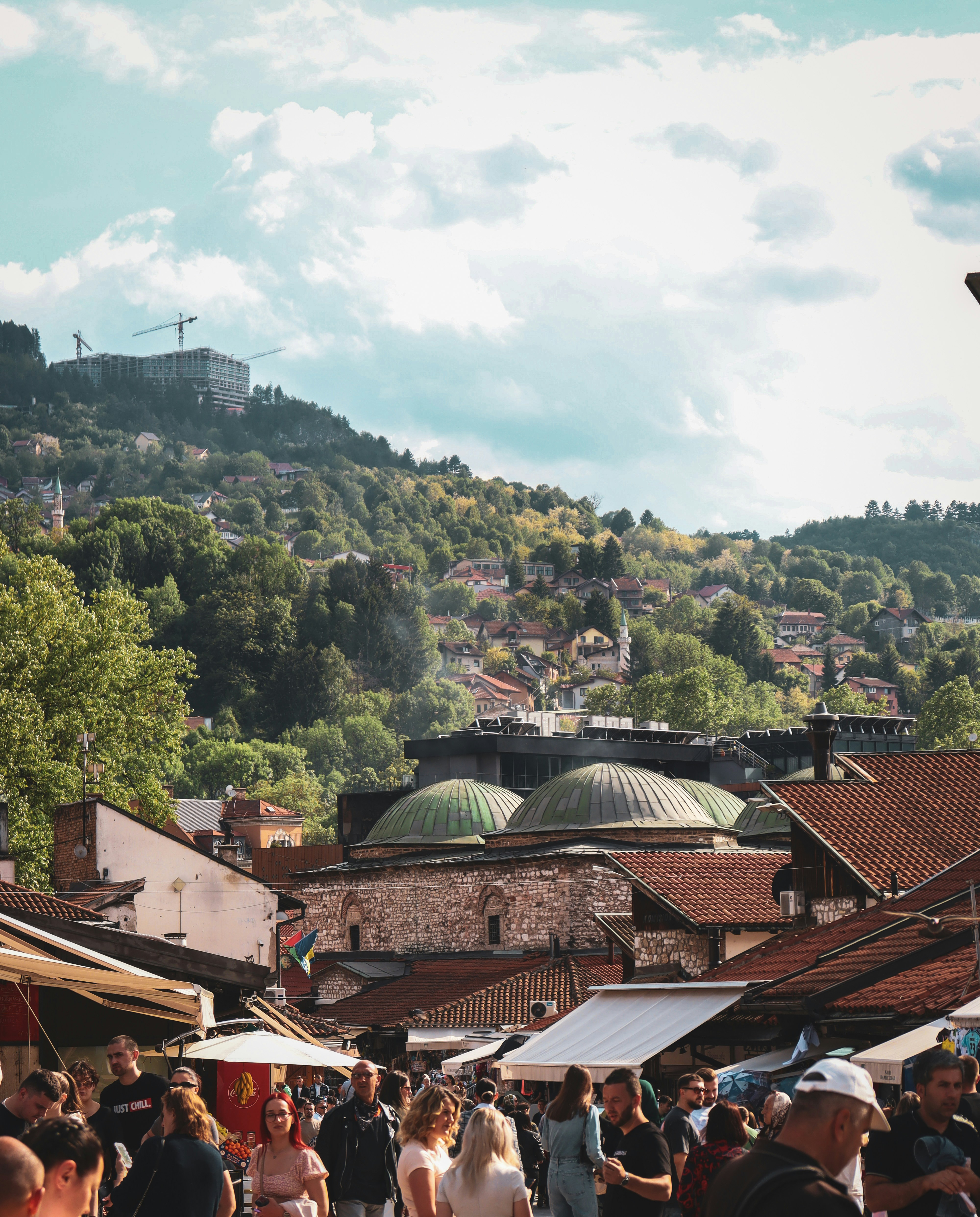Busy Baščaršija marketplace in Sarajevo's old bazaar with Ottoman domes and the forested hills of Bosnia in the background