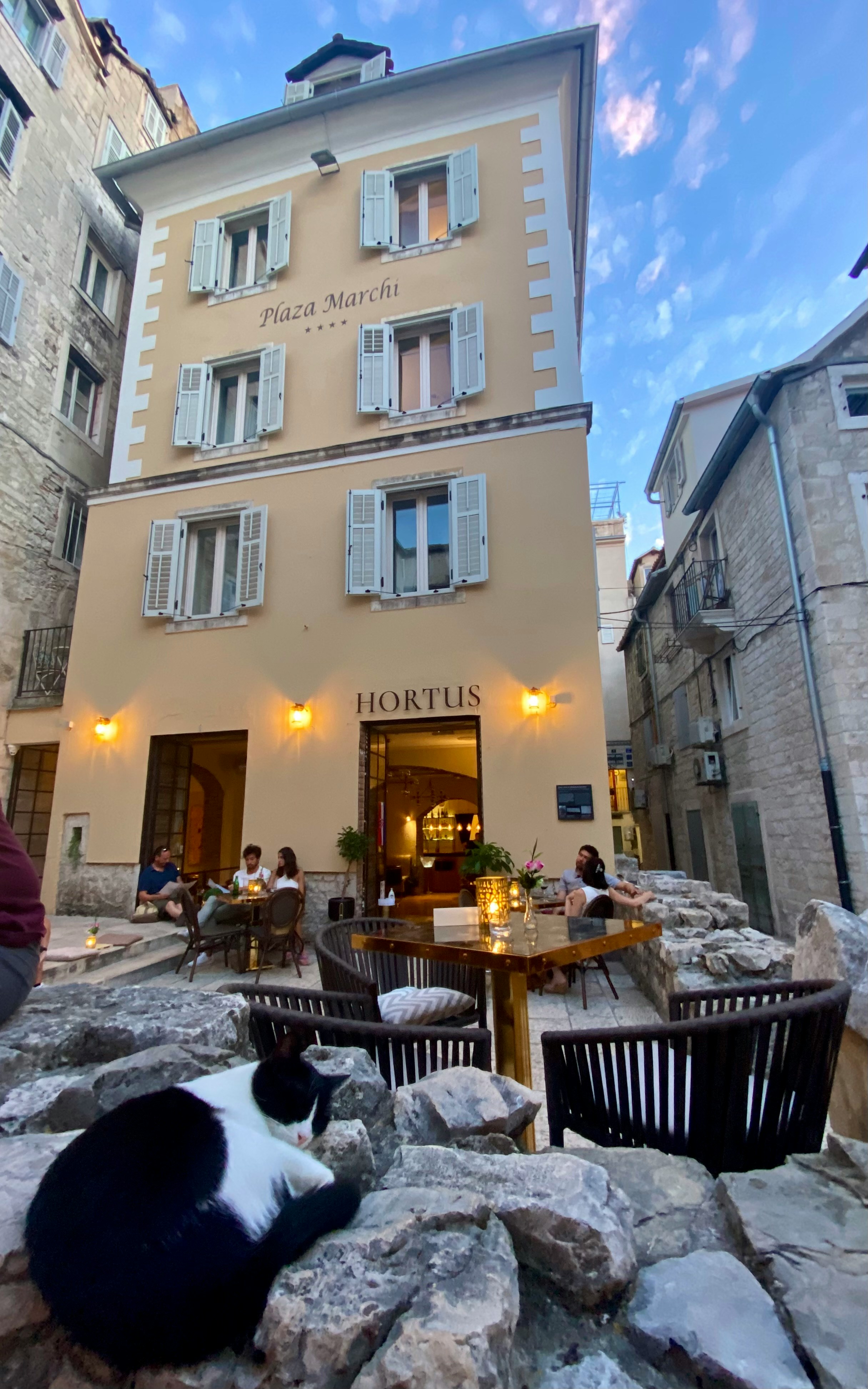 Hortus restaurant terrace in Split's Diocletian Palace walls, Croatia, at dusk with stone paving and a cat in the foreground