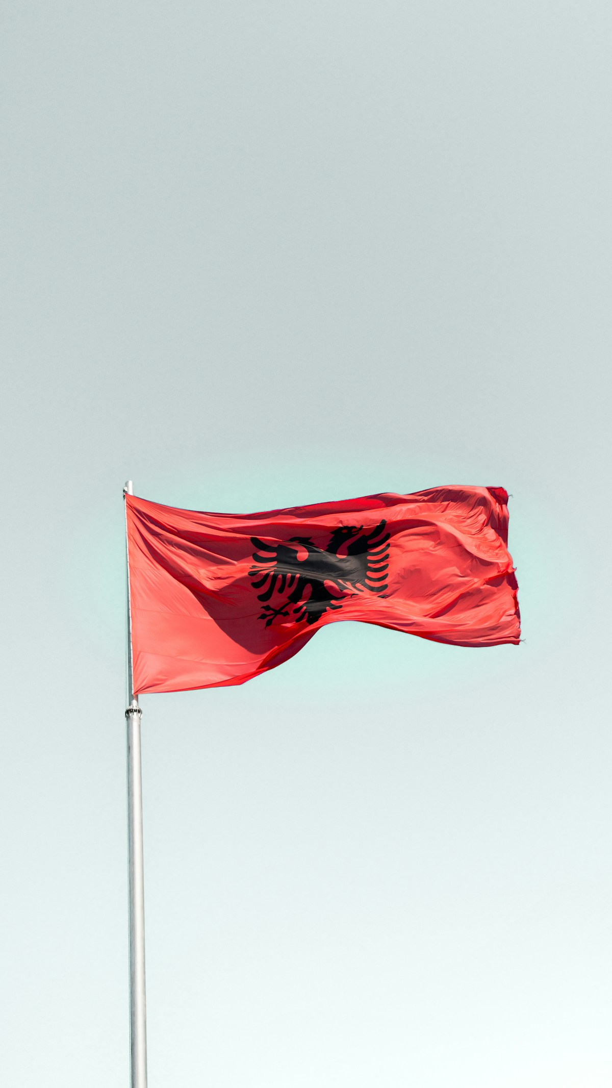 Red Albanian flag flying against a clear blue sky, Tirana, Albania