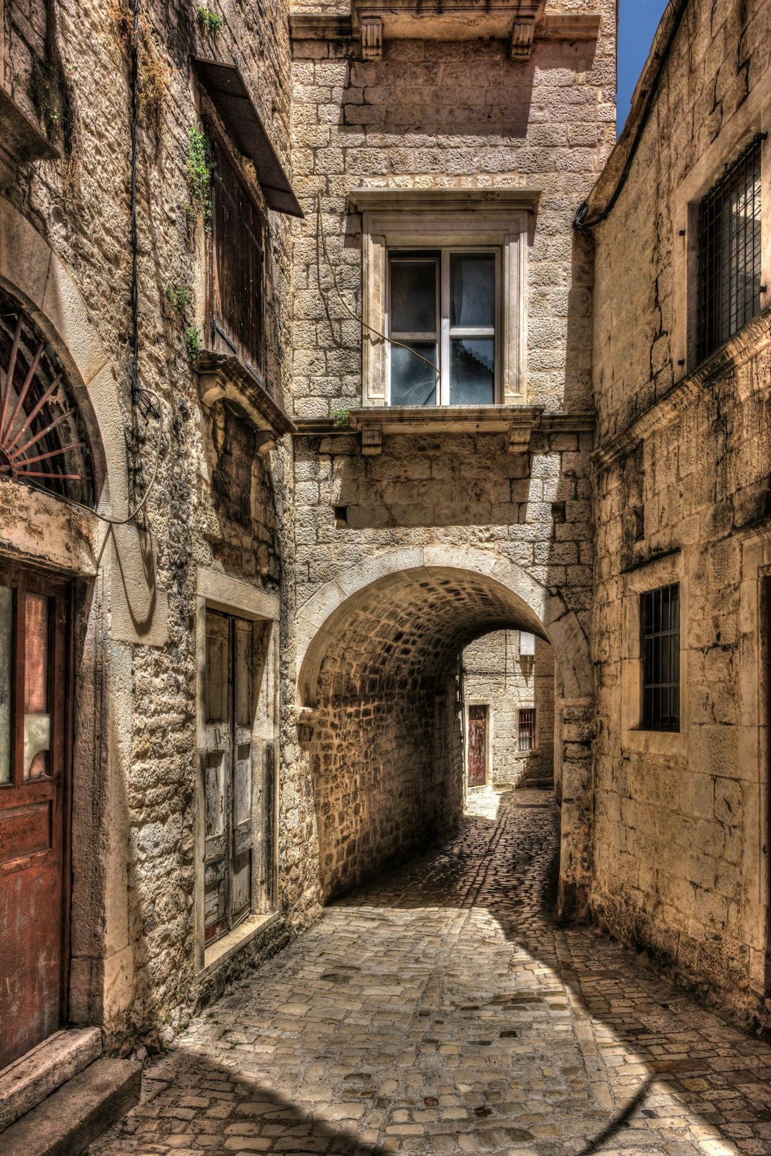Narrow medieval stone alleyway with arched passageway in Trogir old town, Croatia