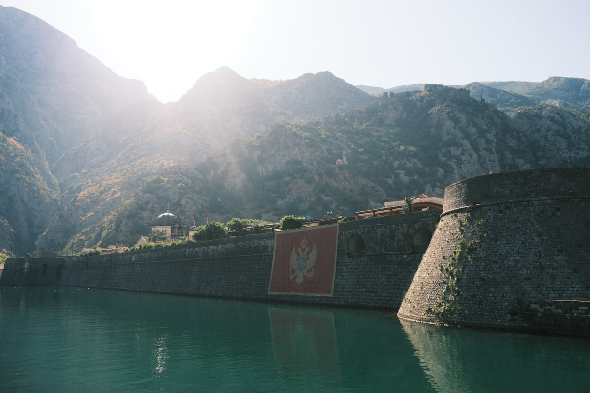 Ancient fortress walls of Kotor with the Montenegrin flag beside calm bay water and mountains, Montenegro